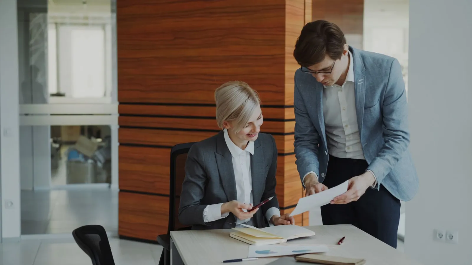 A manager at her desk reviews a document with a colleague who stands beside her